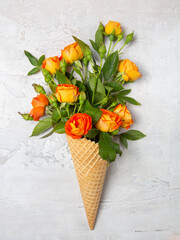 Fresh yellow-orange roses in a waffle cone on a white concrete background. Flat lay. Original packaging of the bouquet.