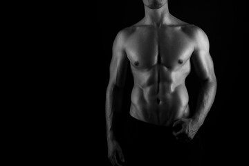 Fototapeta na wymiar Muscular male torso of fit bodybuilder on black background in black and white