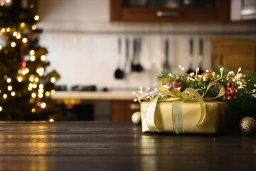 Wooden tabletop with gold gift Christmas decoration and blurred modern kitchen as background.