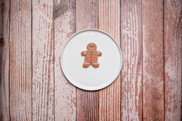 Single Christmas gingerbread man cookie with icing and decorations on a white plate on a weathered wooden table background with copy space and room for text.