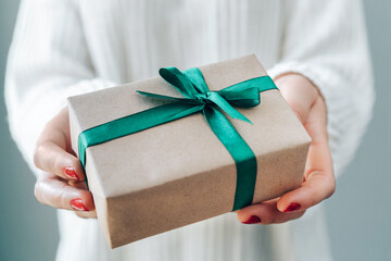 Close up cropped shot of woman hands with red polished nails holding gift box with green satin...