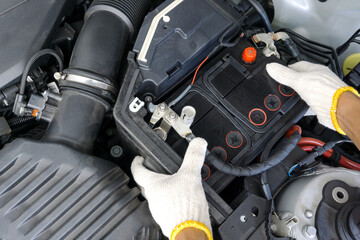 The auto mechanic is replacing the car battery in engine compartment. 