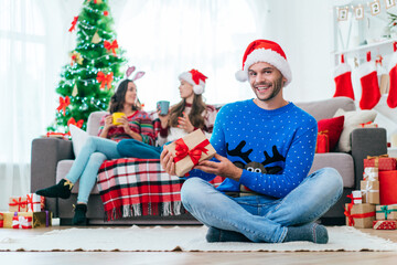 Obraz premium Attractive smiling young man in Santa hat posing with a gift box in hands