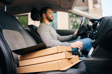 Close-up of bearded delivery man wearing casual clothes driving car delivered hot pizza to customer. Concept of fast online delivery around the city.