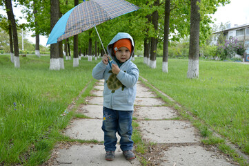 A boy in a blue jacket and an open umbrella stands on the autumn path in the afternoon.