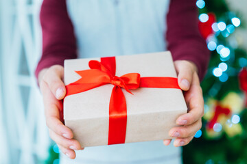 Close up cropped shot of man hands holding gift box with the Christmas tree on the background