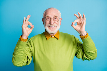 Photo of pensioner old man raise two arms showing okey wear spectacles green sweater isolated blue...