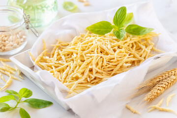 Fresh homemade short twisted pasta Trofie - typical of Liguria Region in Italy - with basil, olive oil and pine nuts at the background