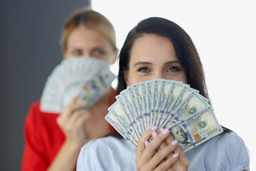 Two smiling women covering face with fan of one hundred dollar bills. Easy money how to make them...