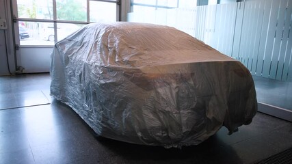 The new car is covered in fabric before the presentation of the gift at the car dealership. A moment of intrigue of surprise at the celebration.