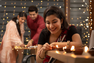 YOUNG WOMAN LIGHTING DIYAS IN OFFICE WITH COLLEGUES IN THE BACKGROUND WITH DIYAS	