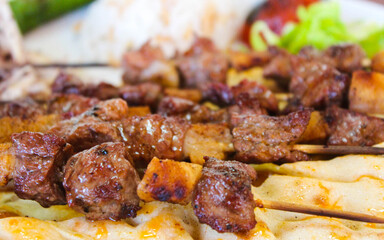 Close up of grilled small pieces of meat on wooden skewers, Turkish traditional food on a plate, Turkish kebab on a plate