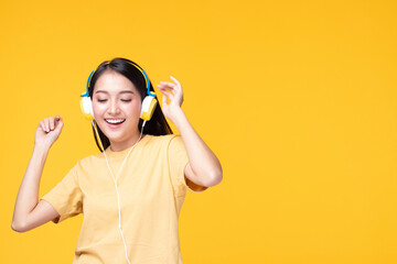 Beautiful young asian woman joyful listening to music on headphones isolated on pastel yellow wall background studio portrait.