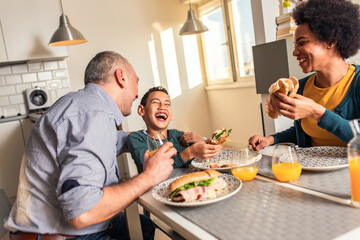 Smiling mixed race family sitting at the kitchen table having breakfast at home.	