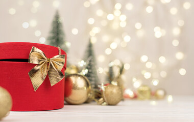 Red Christmas gift box with a gold bow on the background of bokeh, Christmas trees and toys