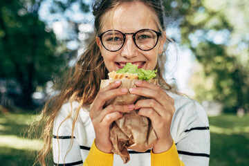 Closeup portrait of a happy student female has lunch with a healthy sandwich outdoors. A blonde...