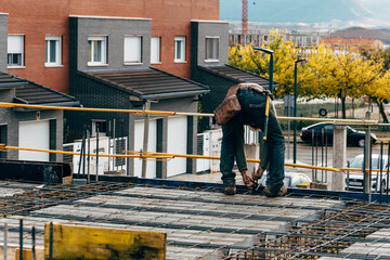 Construction worker working on a reinforced concrete slab. He is tying up steel reinforcements with wires
