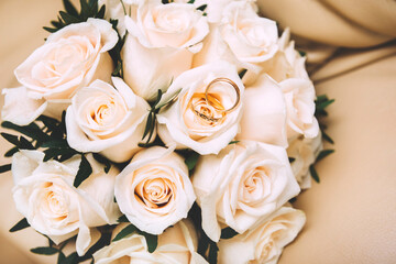 wedding bouquet of white roses with  gold wedding rings on a beige background, flowers
