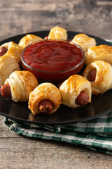 Pigs in blankets. Mini sausages wrapped in puff pastry with ketchup sauce on wooden table
