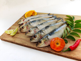 Close up view of Fresh Indian oil sardine on a wooden pad,Decorated with herbs and Vegetables.White Background.