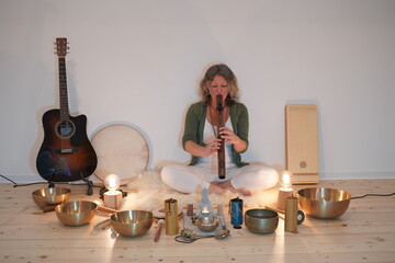 Woman sitting with a native Indian flute for a sound healing session with many sound healing instruments in front of her like singing bowls, koshi chimes, drum, sansula and zimbel.