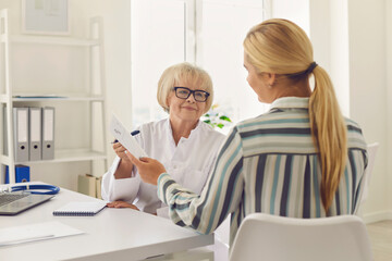 Obraz premium Senior female doctor prescribes medication and gives a prescription to the patient.