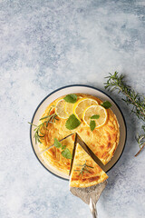 Lemon vanilla cheesecake decorated with rosemary, mint and lemon slices. Ricotta no crust cheesecake or casserole. Blue concrete background. Top view.