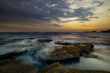 Calm ocean long exposure. Stones in mysterious mist of the sea waves. Concept of nature background. Sunset scenery background. Mengening beach, Bali, Indonesia.