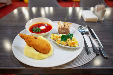 Set lunch on the table in the restaurant. Red borscht, mashed potatoes with chicken nuggets, Olivier salad and cutlery.