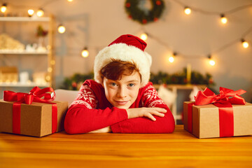 Portrait of a happy boy leaning on his hands on the table among his Christmas presents.