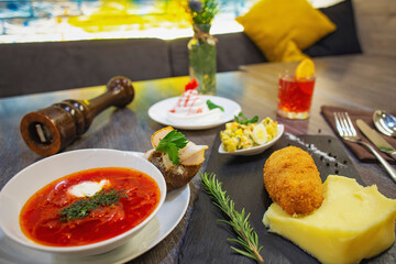 Set lunch on the table in the restaurant. Red borscht, mashed potatoes with chicken nuggets, Olivier salad and cutlery.