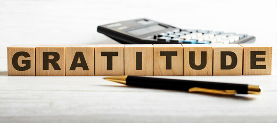 The word GRATITUDE is written on wooden cubes between a calculator and a pen. Business concept.