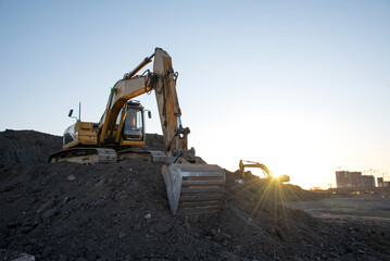 Excavator on earthworks at construction site on sunset background. Backhoe loader during recycling...