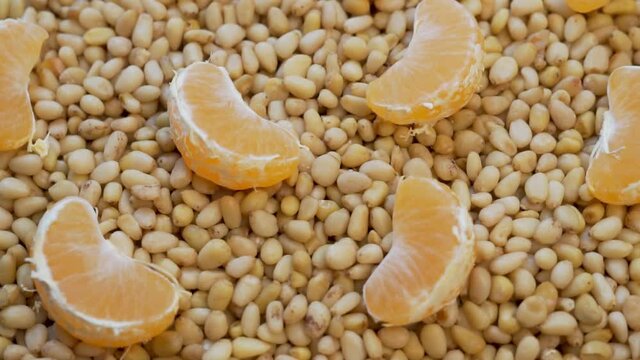 Peeled Pine Nuts and Tangerine Fruit Slices, Closeup, Rotate. The Concept of Healthy Vegan Vitamin Food. Background of Pine Nuts and Tangerine Slices.