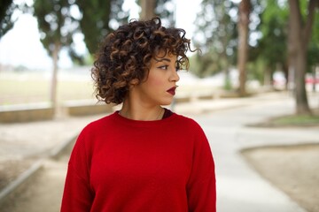 Fototapeta na wymiar Close up side profile photo Young beautiful Arab woman standing outdoors wearing red sweater ready to have a walk.