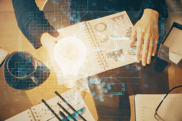 Bulb hologram over hands taking notes background. Concept of idea. Double exposure