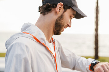 Pleased unshaven guy looking at wristwatch while working out