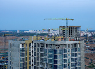 View on the large construction site at urban area in the evening. Tower cranes in action with machinery and builders. Multi-storey residential Building is being constructed use of crane.