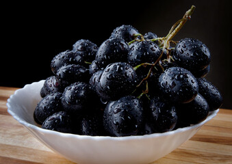 White plate with black grapes. Water drops on ripe grapes.