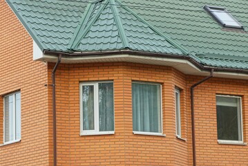 brown bricks wall of a private house with white windows under a green tiled roof
