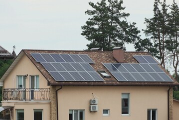 Fototapeta premium one large brown private house with tiled roof windows and gray solar panels against the sky and pine trees