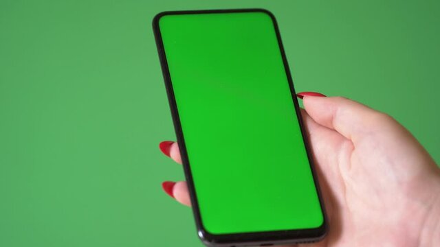 Woman hand holding the smartphone on green screen chroma key background. Mobile phone mock-up for your product. The iPhone Xr model in vertical orientation portrait mode