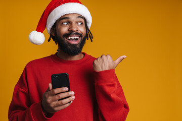 Happy african american guy pointing finger aside while using cellphone