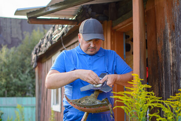 Close-up, funny fat man in blue overalls and a baseball cap, repairing a trimmer, against the...
