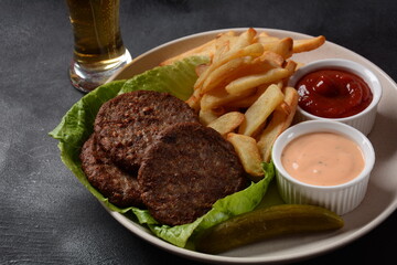 Burger meat steaks french fries and salad on black background