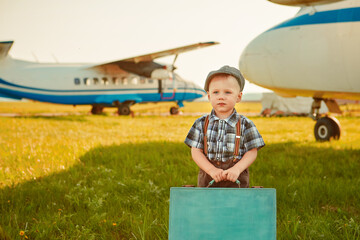 A cute little boy stands next to the propeller of an old airplane on a Sunny day.