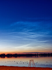 Fototapeta na wymiar Noctilucent clouds also known as a night shining clouds over a lake.