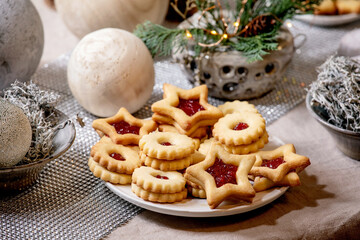 Homemade traditional Christmas Linz shortbread biscuits cookies with red jam on plate. Trend Wooden eco-friendly xmas decorations on linen tablecloth. Holiday table setting.