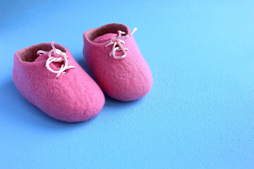 Fototapeta na wymiar Felted woolen pink booties for a newborn on a blue background