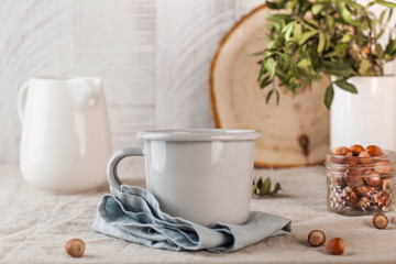 A metal mug on a linen tablecloth, a white jug of milk on the back. Still life in rustic style.